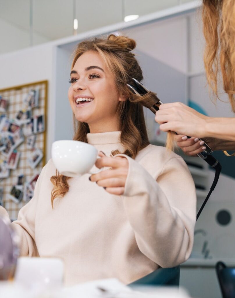 Blonde girl indoors in beauty salon with hairdresser.